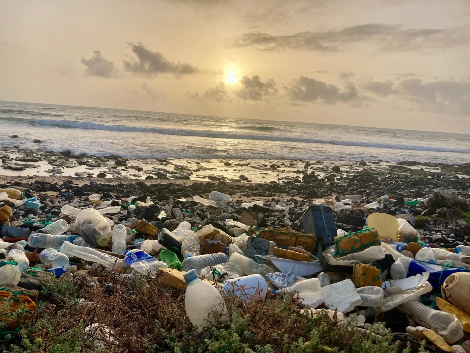 Orilla al atardecer cubierta de botellas y residuos plásticos